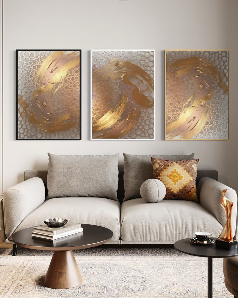 Set di tre stampe astratte incorniciate con sfumature oro e grigio su fondo chiaro.